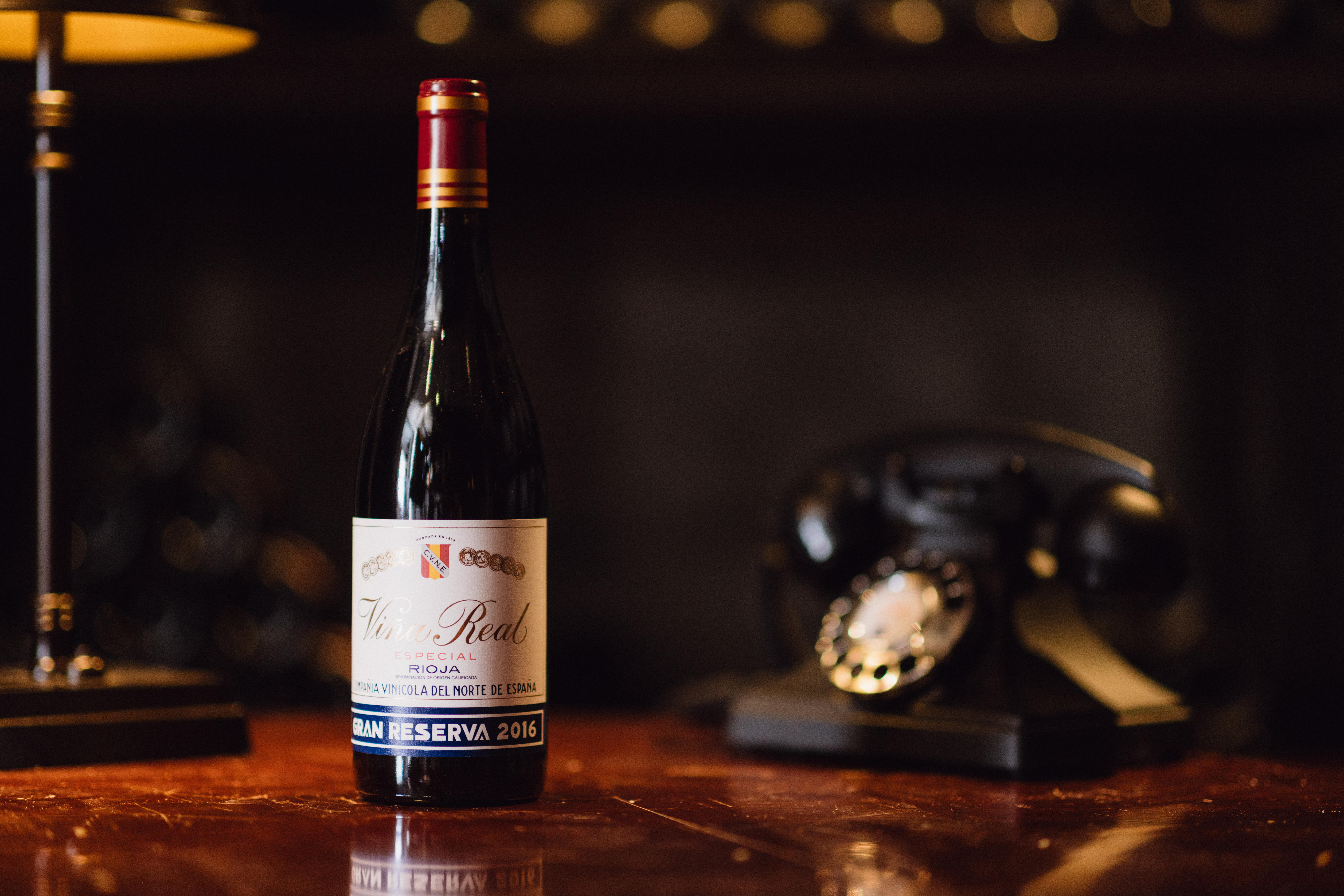 A bottle of 2016 Viña Real Gran Reserva (CVNE, Rioja, Spain) sits on a polished wooden surface in warm, ambient lighting.