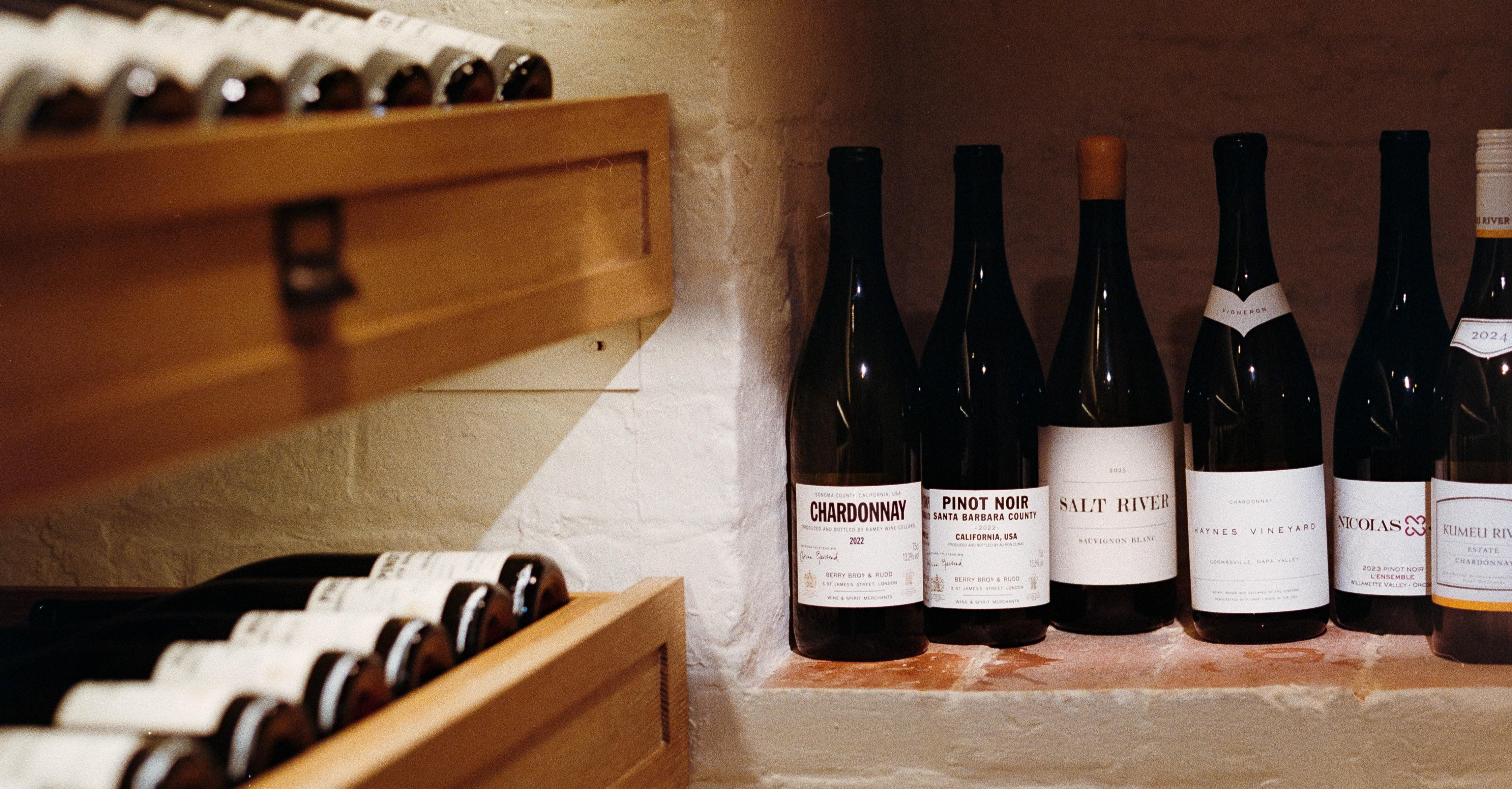  A selection of wine bottles in a softly lit cellar, with wooden racks and stone walls creating a refined storage setting.