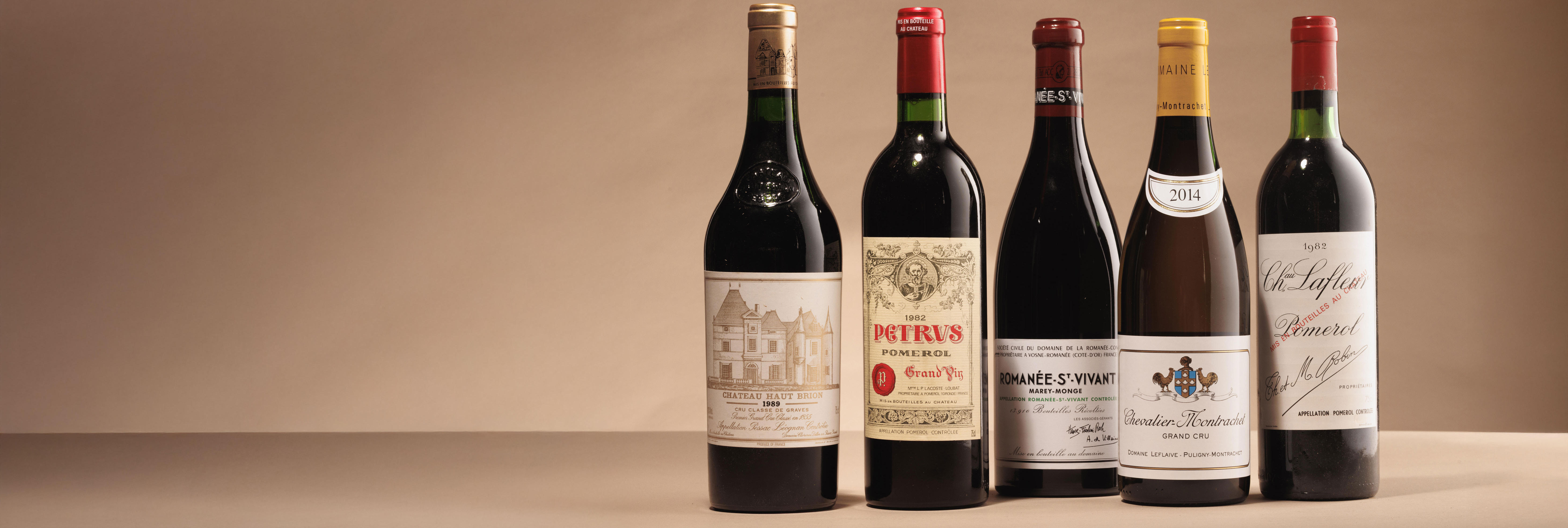 Fine wine bottles, including Château Haut-Brion, Pétrus, Romanée-St-Vivant, Chevalier-Montrachet, and Château Lafleur, displayed against a soft beige backdrop — representing rare and collectable wines available at Berry Bros. & Rudd Auctions.