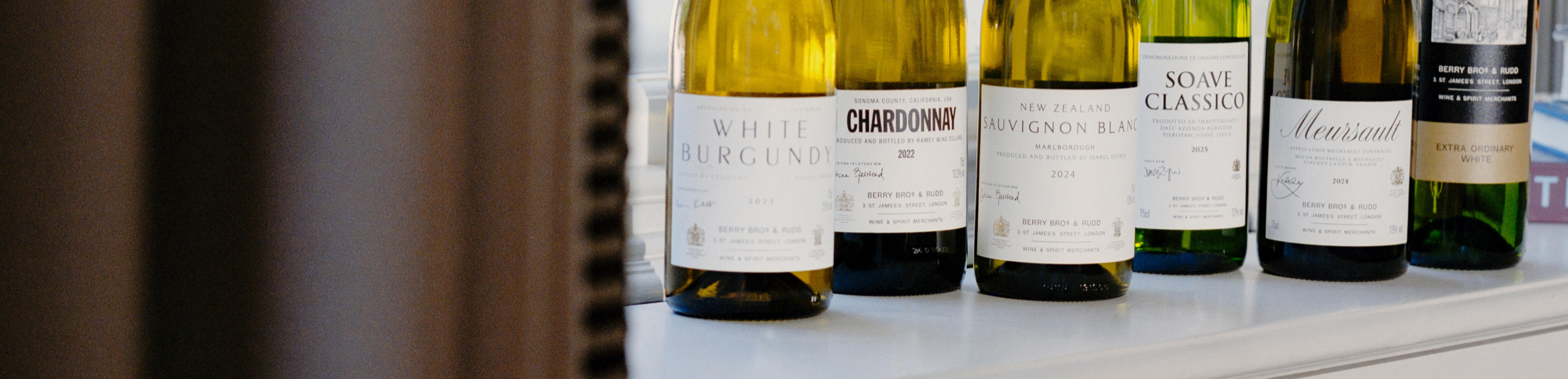 6 bottles of Berry Bros. & Rudd Own Selection white wines sitting on a window sill with a curtain drawn to them on the left.