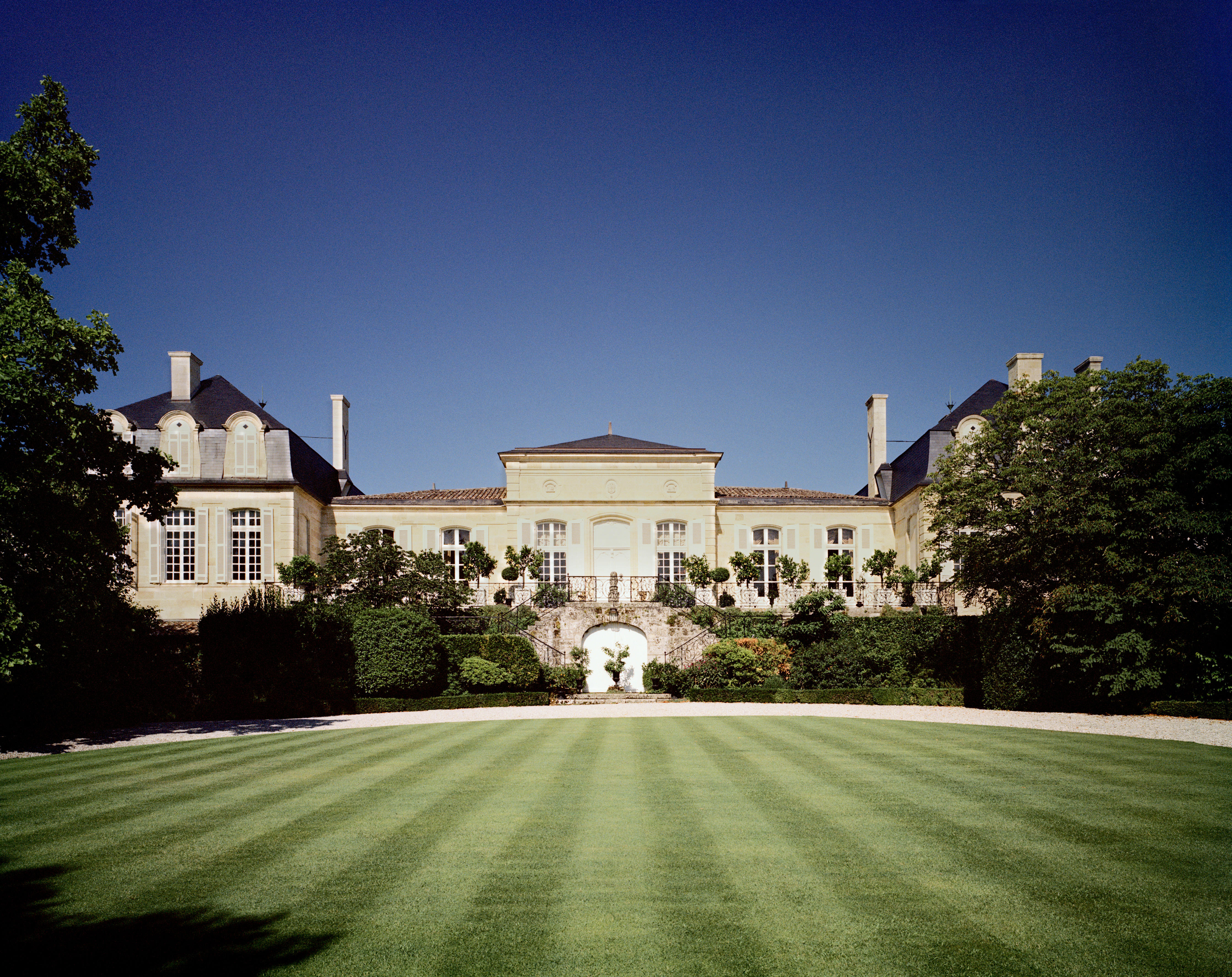 Château Léoville Barton in St-Julien, Bordeaux, with manicured lawns, symmetrical architecture, and a clear blue sky.