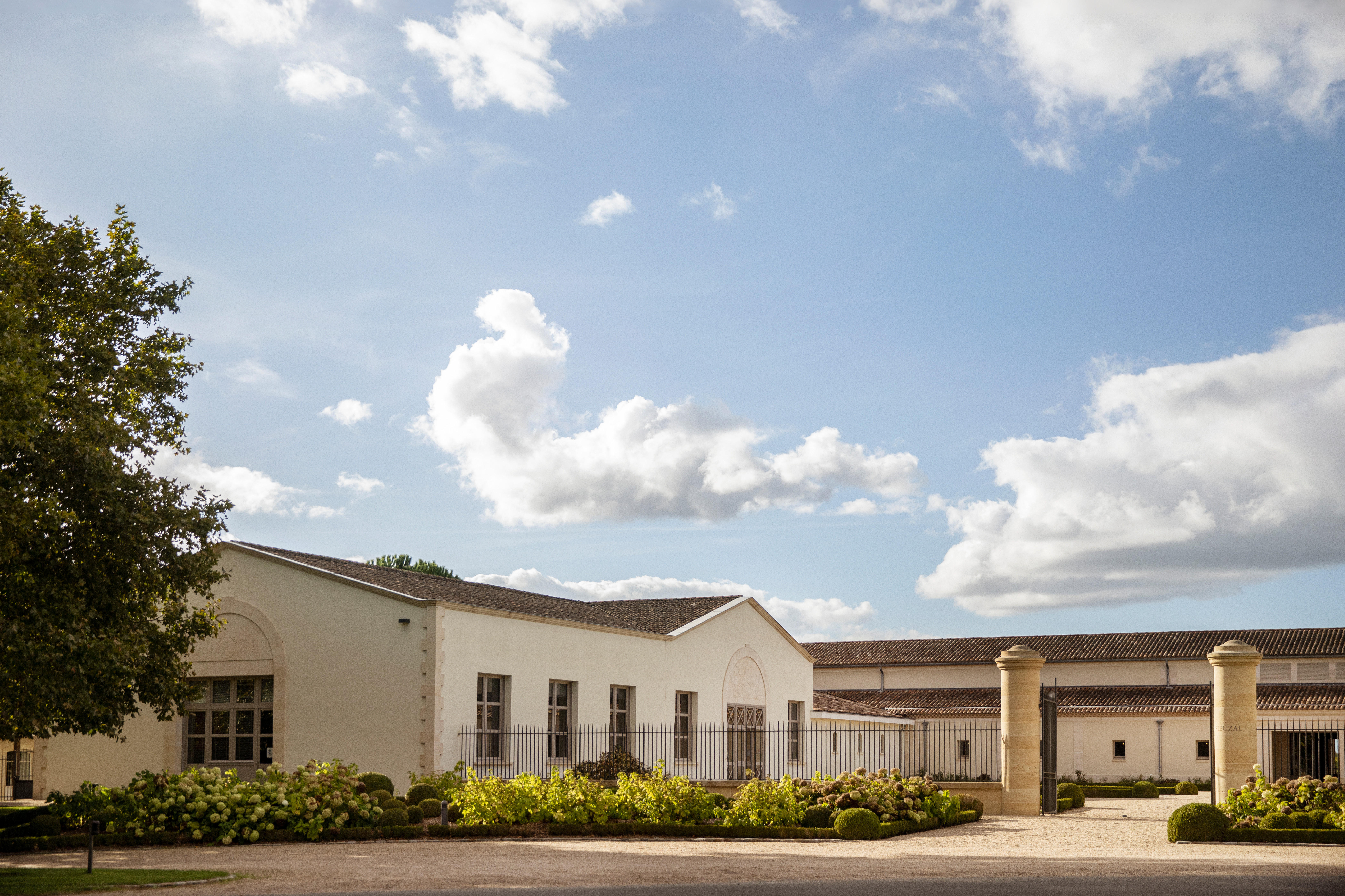 The entrance and cellars of Château de Fieuzal in Pessac-Léognan, surrounded by manicured gardens under a bright blue sky.