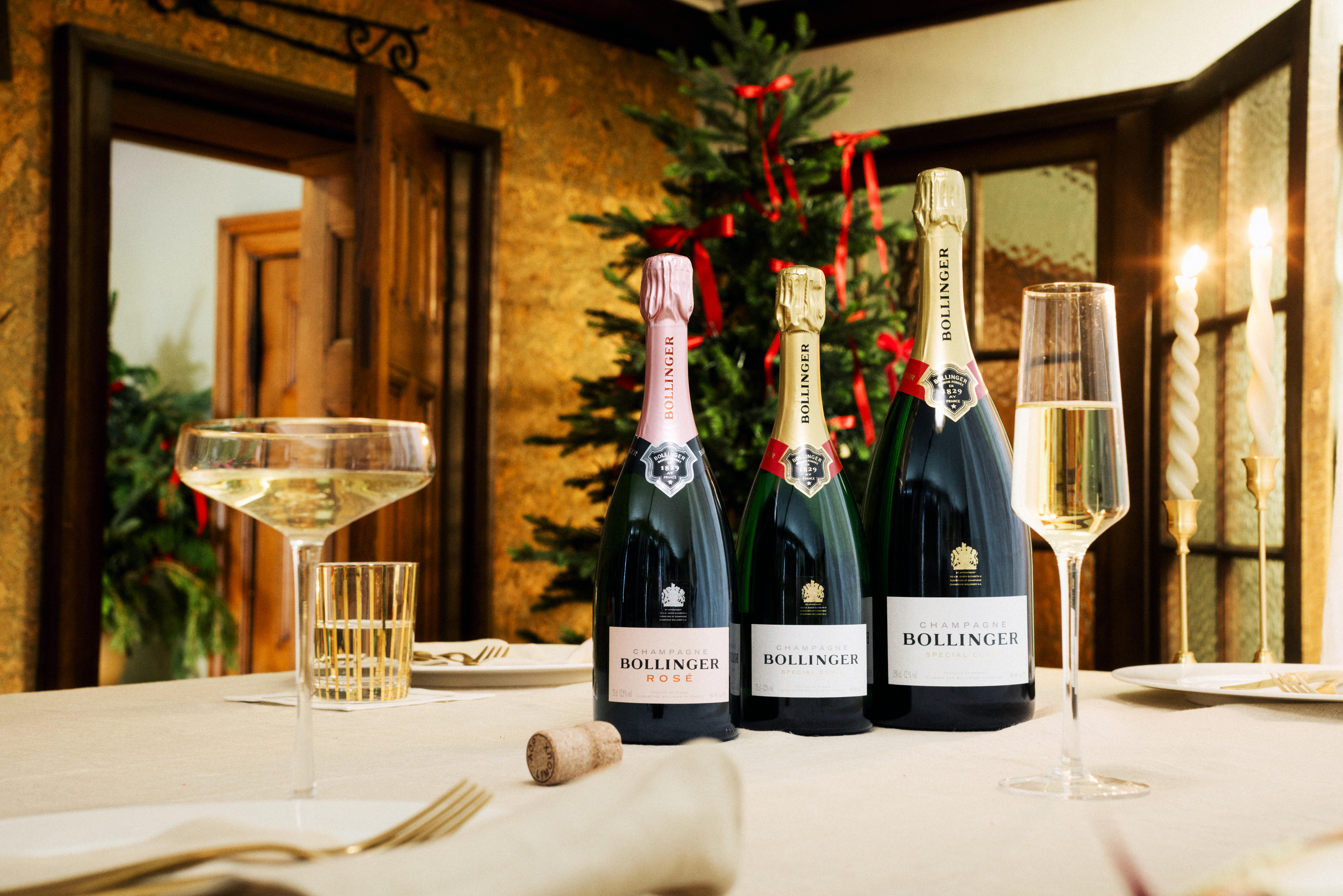 Three bottles of Champagne Bollinger – Rosé, Special Cuvée and La Grande Année 2015 – displayed on an elegant table set for a celebration, with Champagne glasses and festive décor in the background.