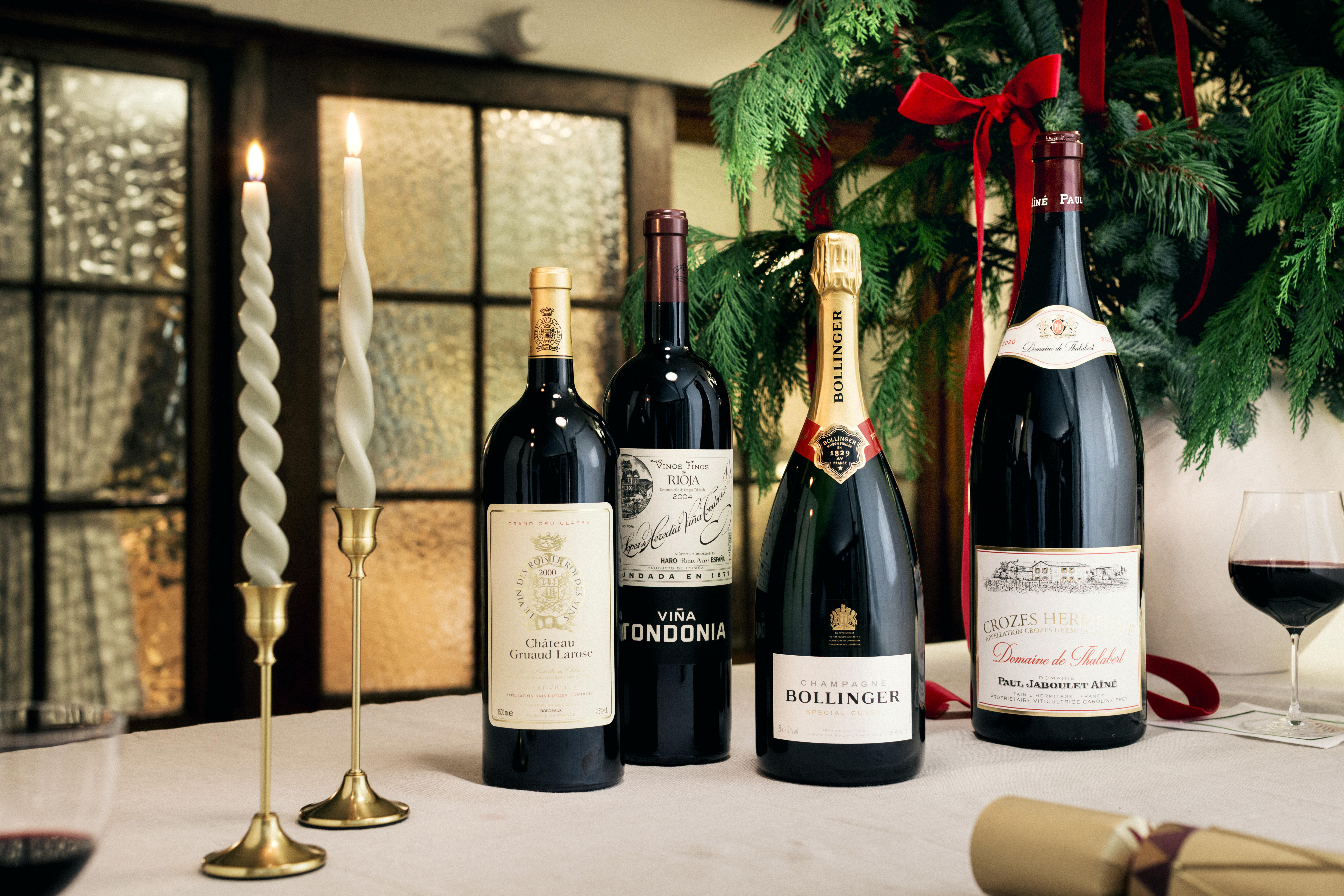 Festive table with magnums and large-format wines, including Château Gruaud Larose, Viña Tondonia, Bollinger Champagne, and Crozes-Hermitage, alongside candles and holiday greenery.