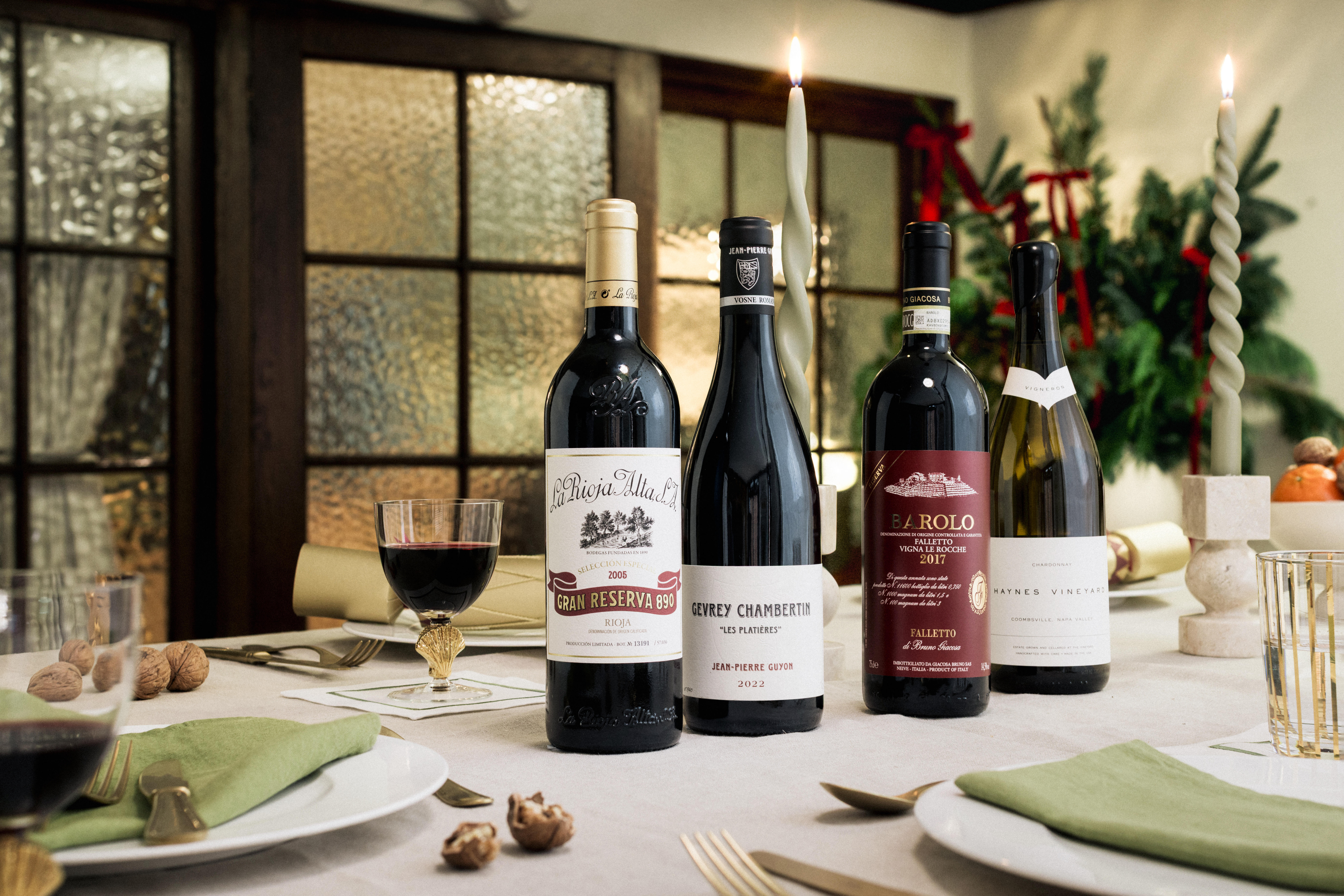 Elegant Christmas dining table with four premium wines: Gran Reserva 904 (2015), Gevrey Chambertin (2019), Barolo (2017), and Château de Sancerre, surrounded by green napkins, gold cutlery, candles, and festive decorations.