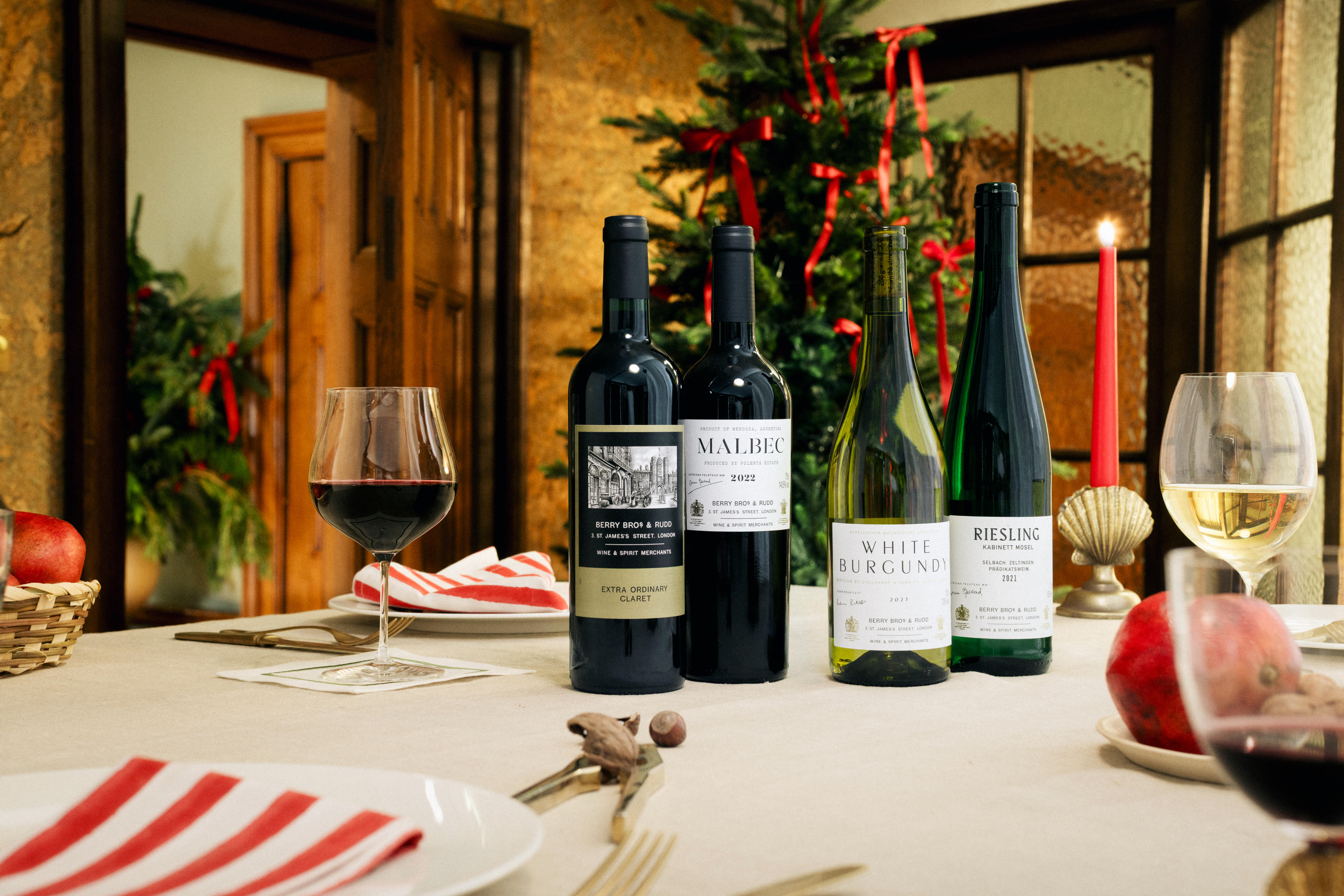 Four bottles of Berry Bros. & Rudd Own Selection wines—two reds and two whites—displayed on a festive dining table with glasses of wine, striped napkins, and Christmas decorations in the background.