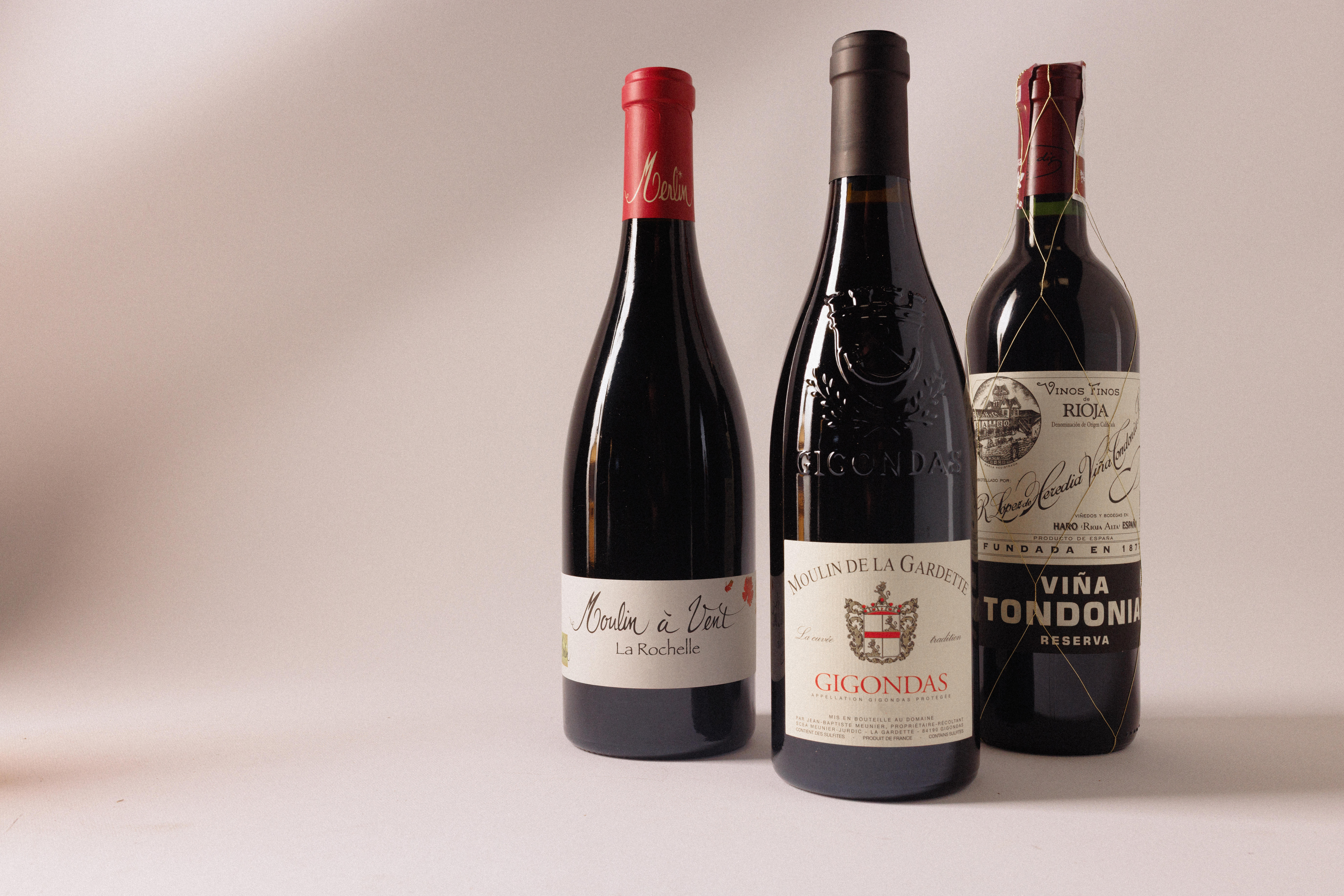 Bottles of red wine against a grey-tan background. 