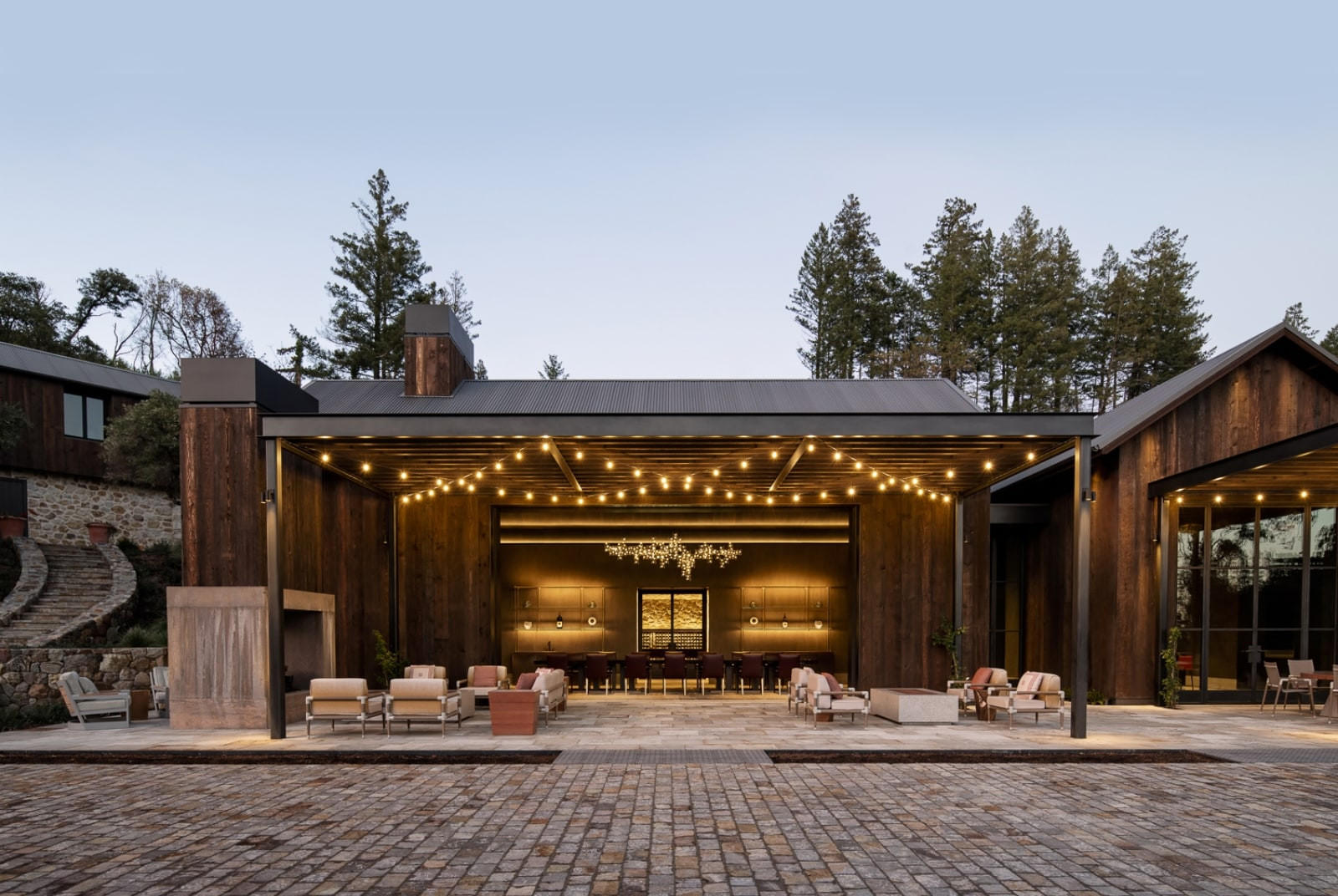 Modern tasting room at Mayacamas Vineyards with warm string lights, rustic wood architecture, and outdoor seating against a backdrop of Mount Veeder forest.