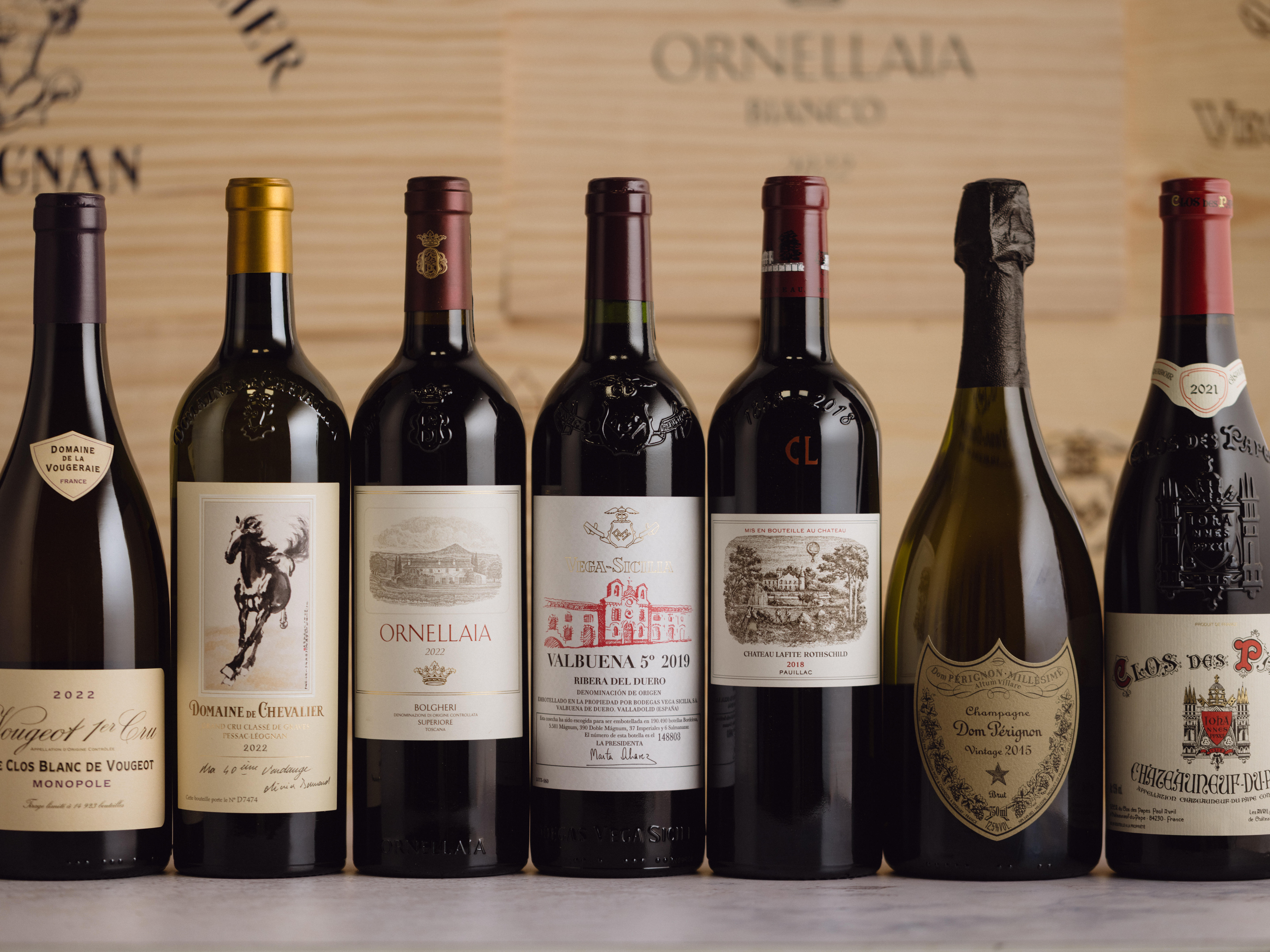 Seven premium wine bottles from Champagne, Bordeaux, Burgundy, Tuscany, Spain, and Napa Valley, including Dom Pérignon and Ornellaia.