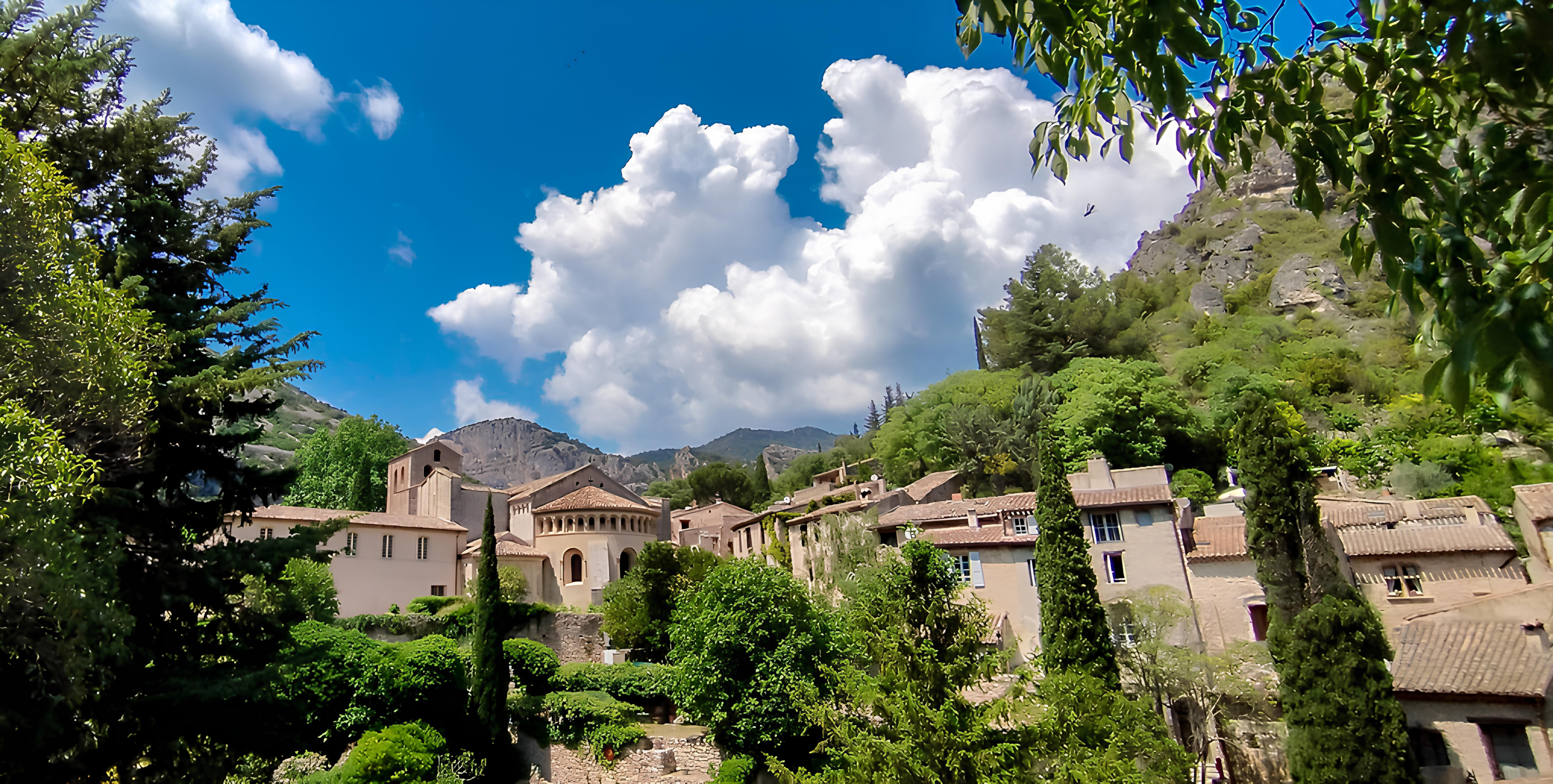 Saint-Guilhem-le-Désert village in Languedoc, surrounded by green hills and limestone cliffs under a blue sky.