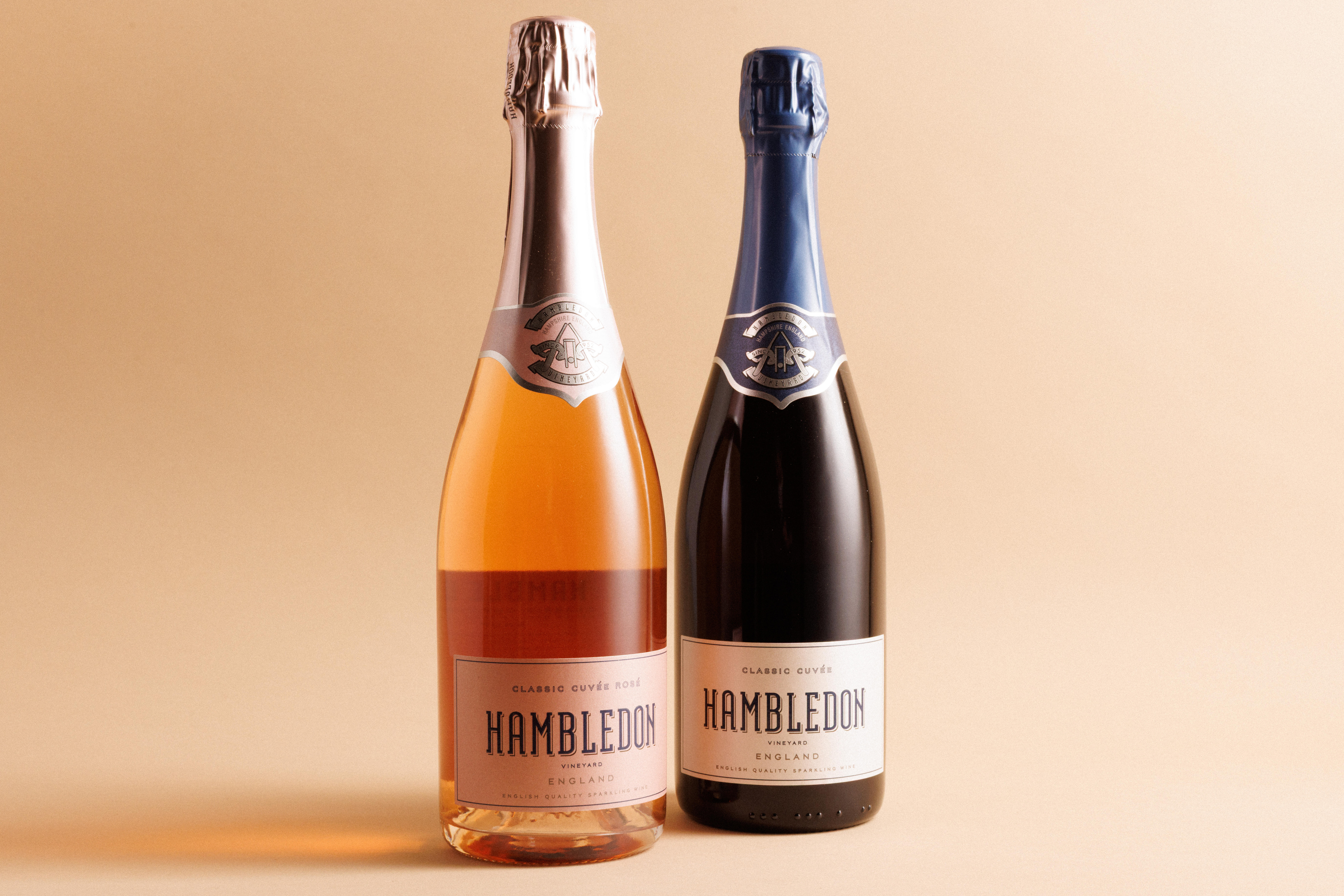 Two bottles of Hambledon sparkling wine: Classic Cuvée Rosé and Classic Cuvée on a beige background.