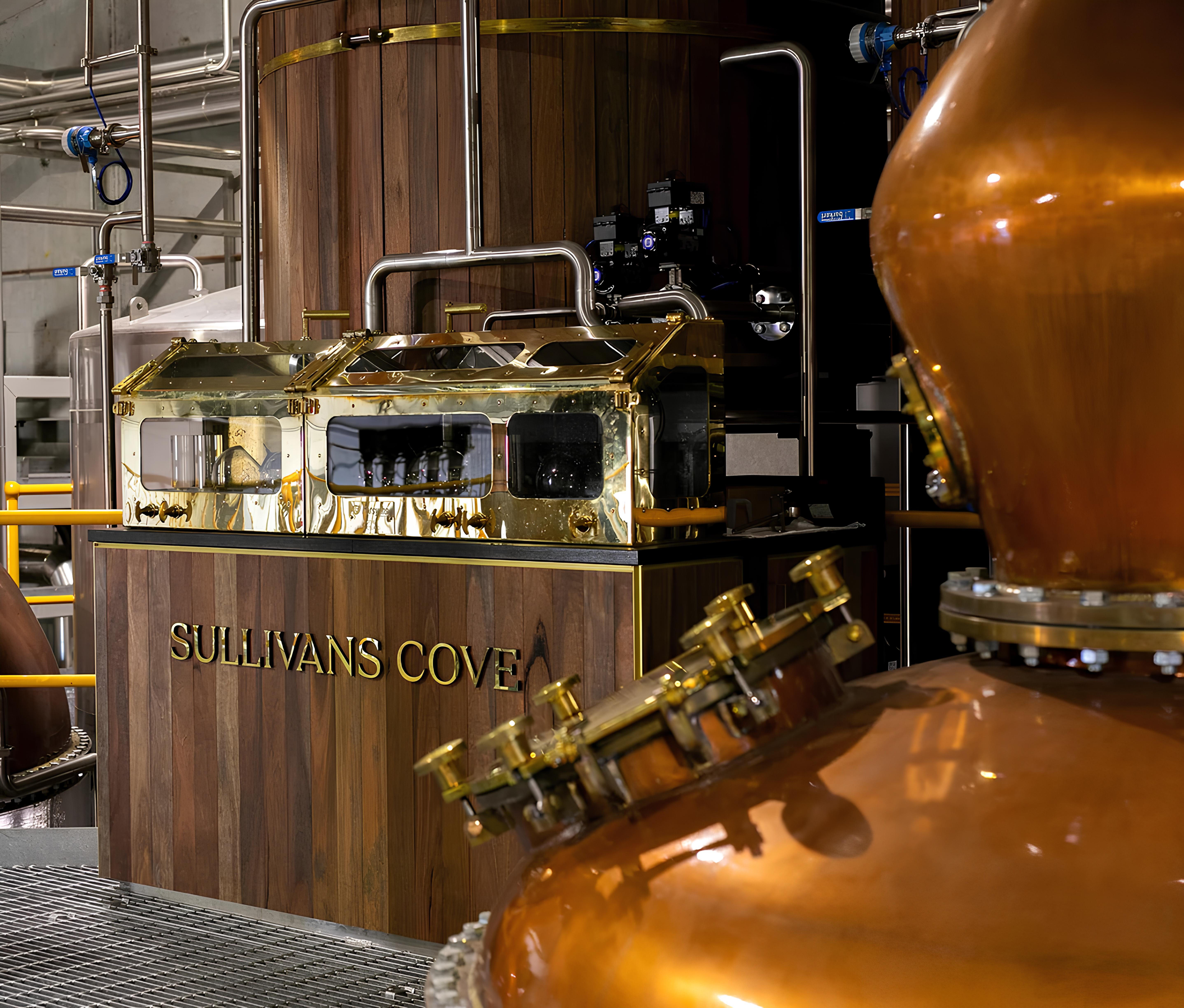 Copper pot stills and a polished brass spirit safe inside Sullivans Cove distillery, with wooden paneling engraved with the distillery name, showcasing traditional whisky-making equipment and craftsmanship.