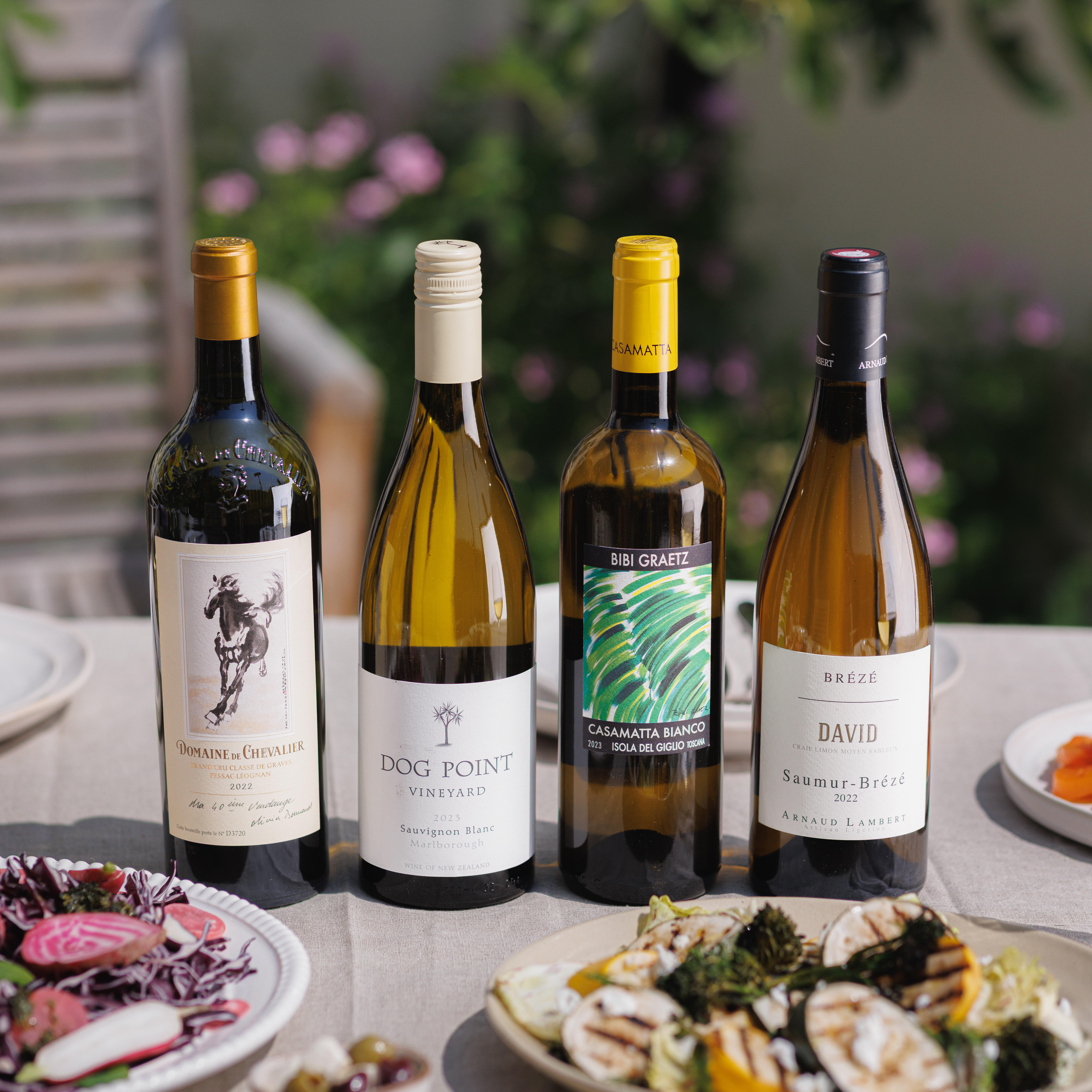 A selection of fine white wines for summer displayed outdoors on a laid table.