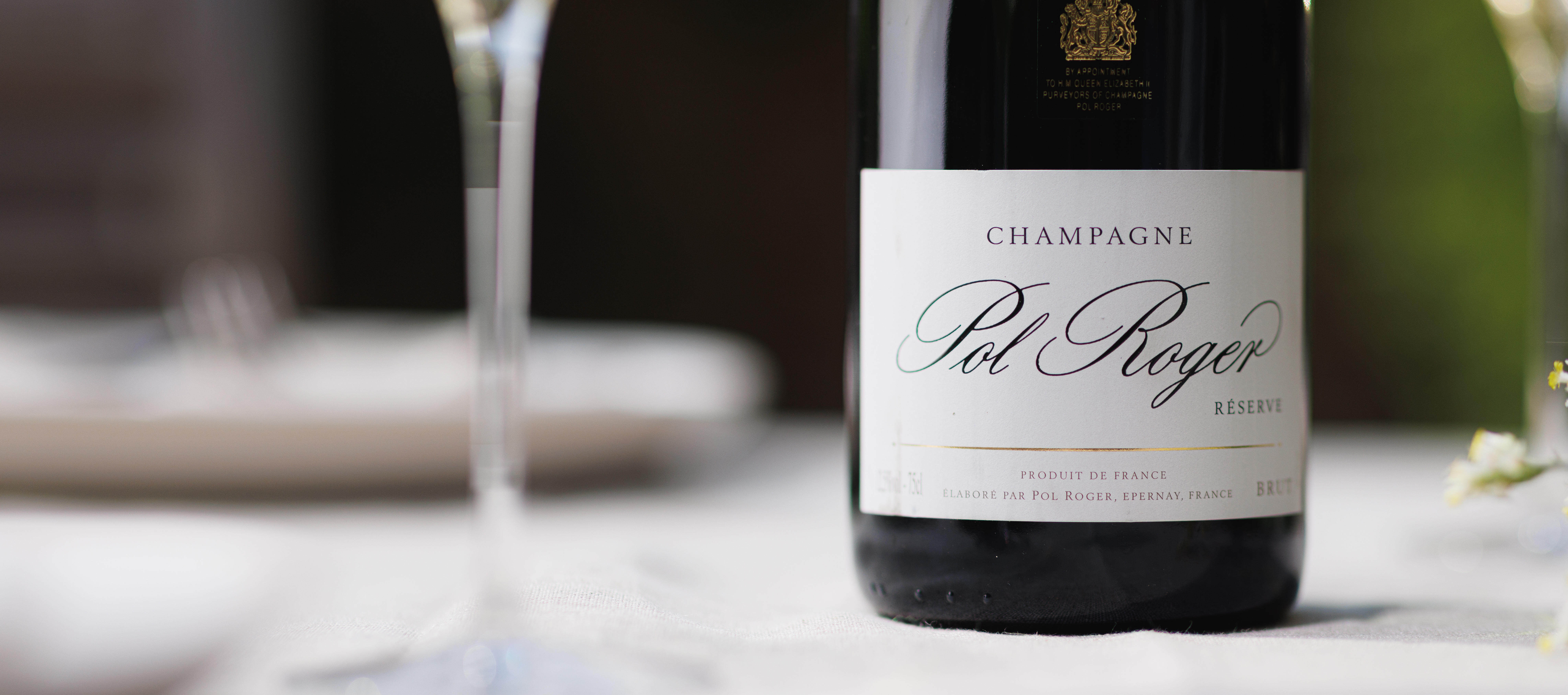 A bottle of Pol Roger Champagne sitting on a white table cloth with flowers in the background. 