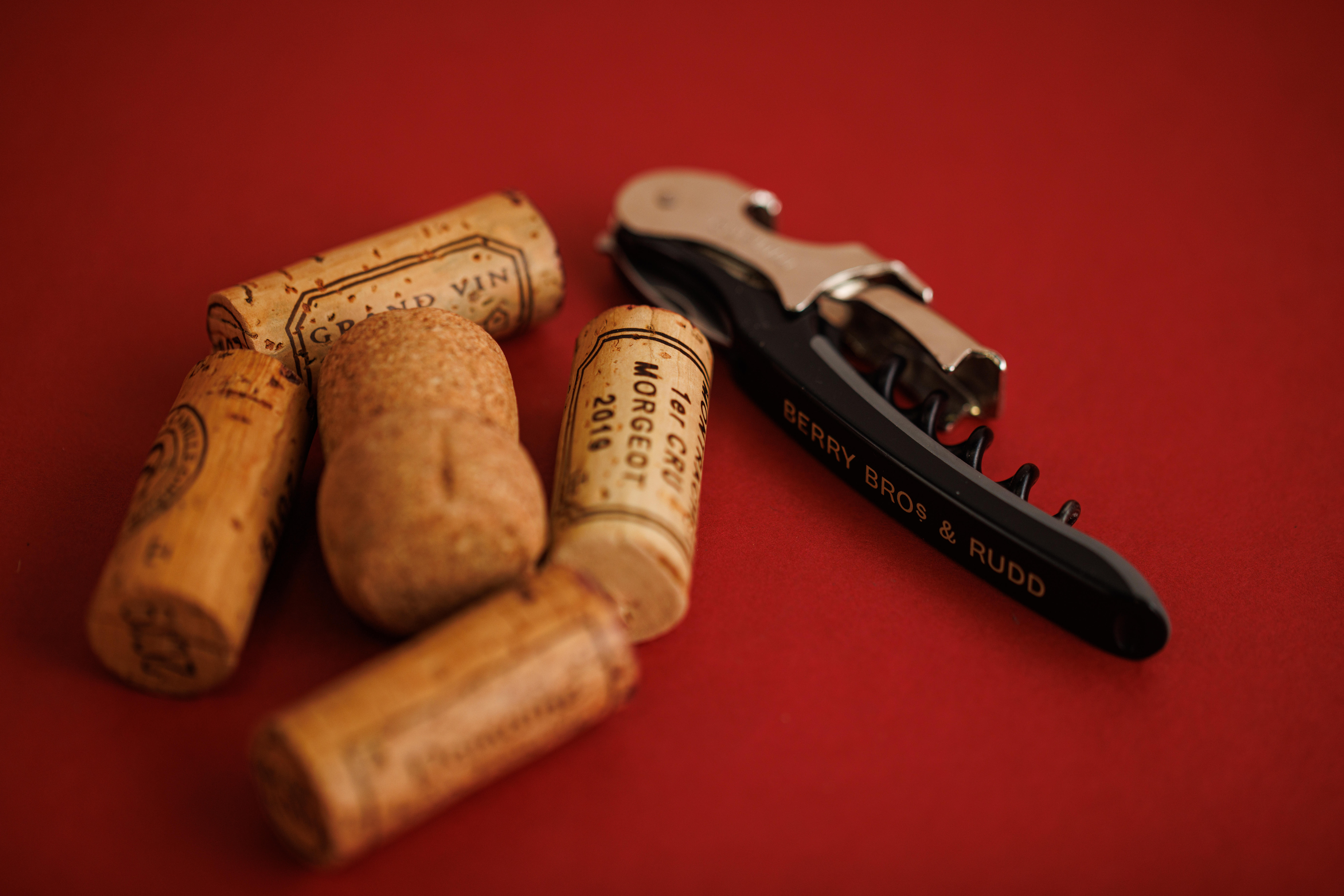 Close-up of a dark green Berry Bros. & Rudd corkscrew lying beside assorted wine corks on a red background.