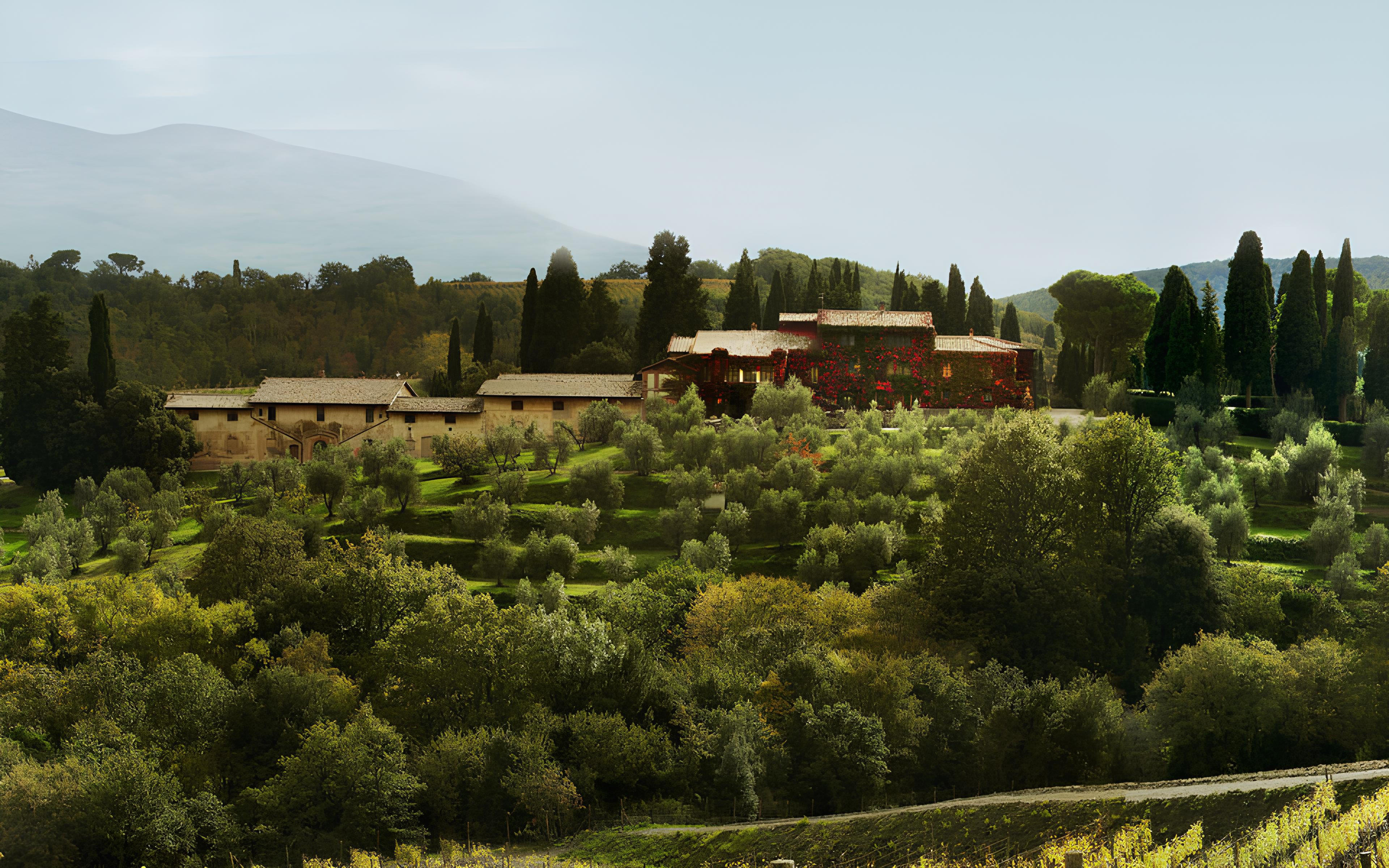 Historic Tenuta Greppo estate of Biondi-Santi in Montalcino, Tuscany, surrounded by rolling vineyards, olive groves, and tall cypress trees under a soft, hazy sky.