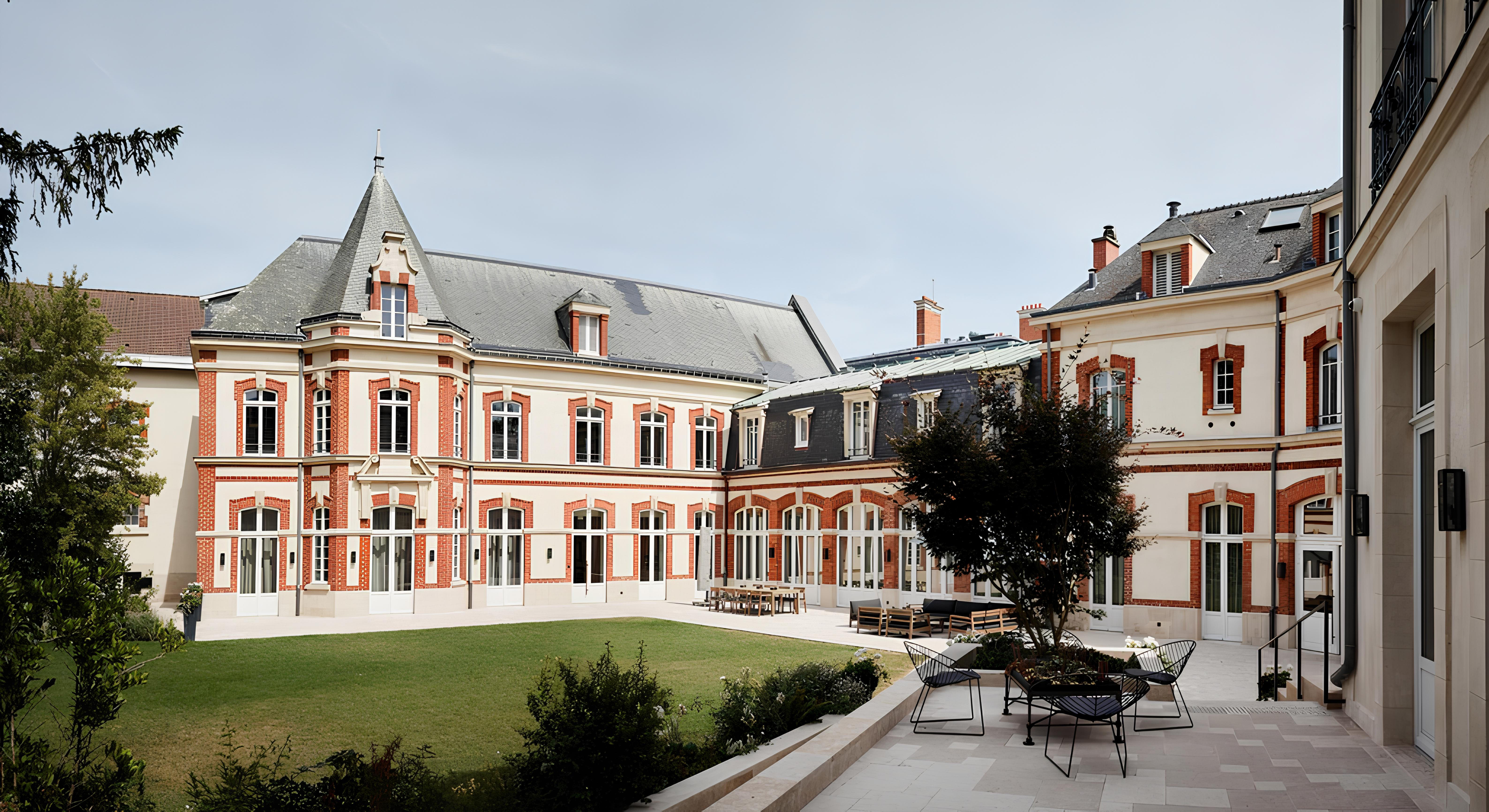 Courtyard of the historic Krug Champagne estate with red-and-white brick architecture, slate roof, and landscaped central lawn under a clear sky.