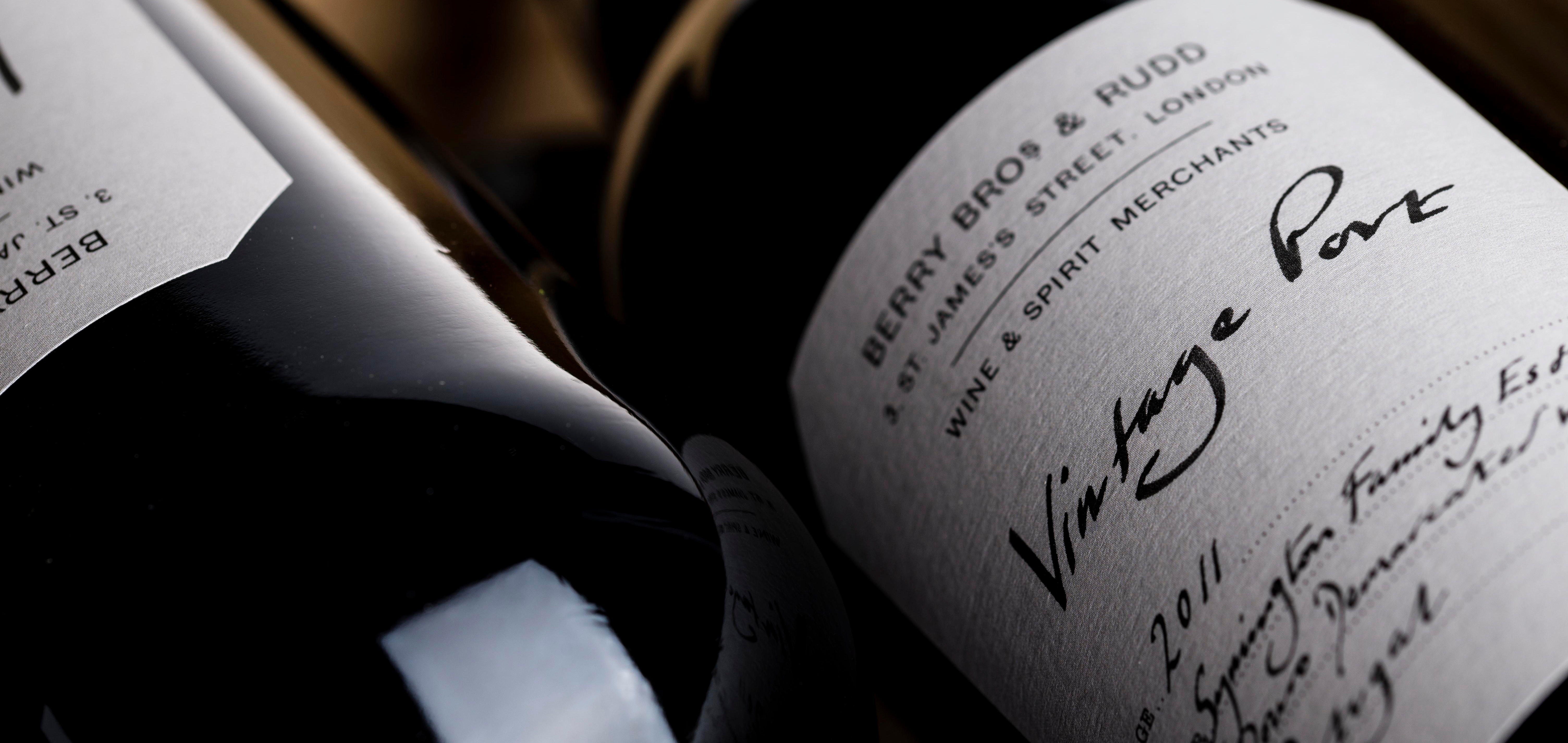 Close-up of two wine bottles lying on their sides, partially visible in soft lighting. The focus is on the label of one bottle, which reads “Berry Bros & Rudd, Wine & Spirit Merchants” and prominently features the handwritten words “Vintage Port.”